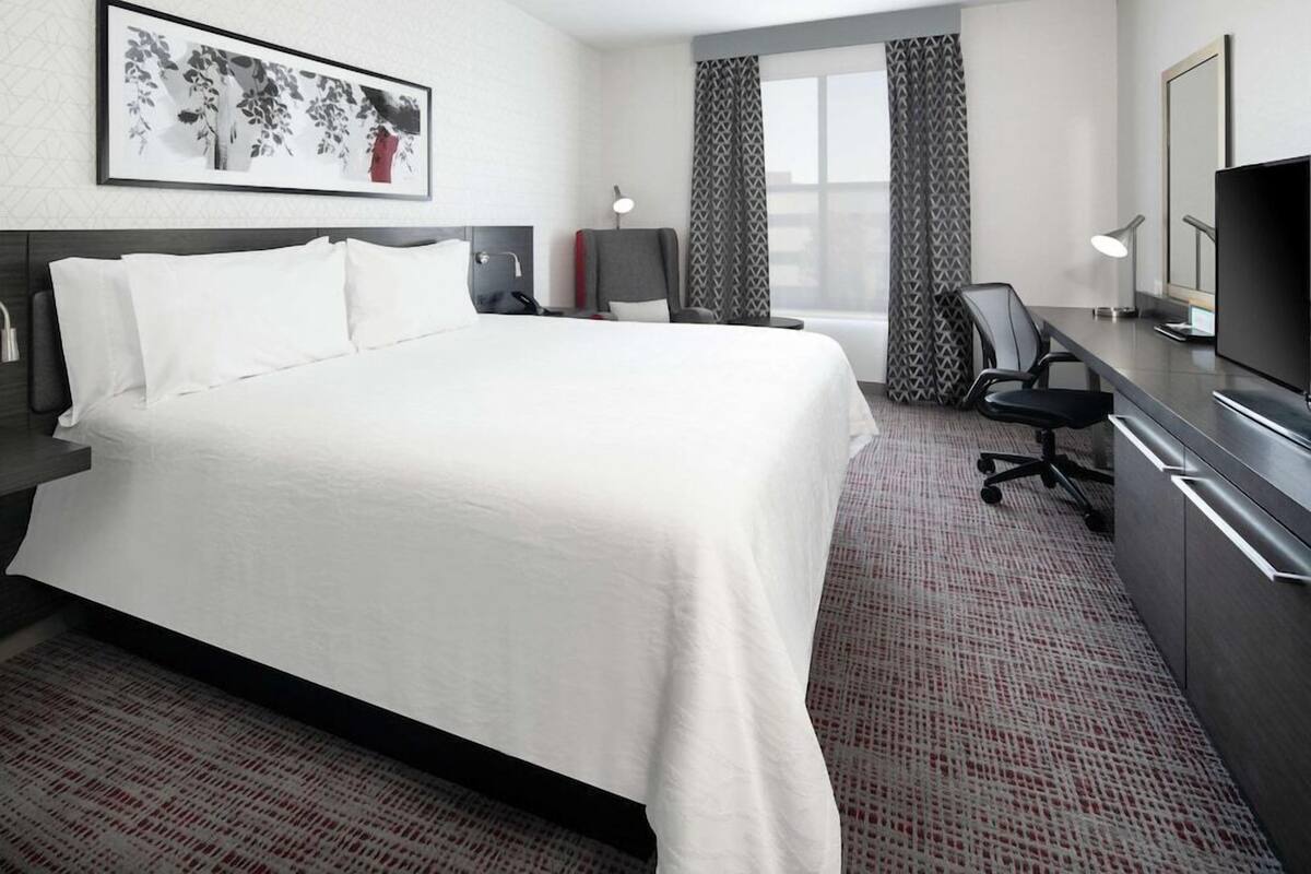 A hotel room with a large bed, a desk with a chair, a television, and a window with curtains.