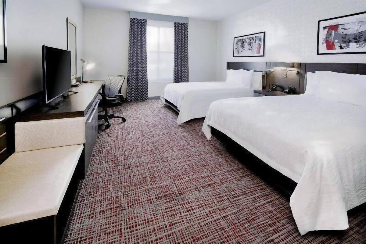 A hotel room with a bed, a desk, a chair, a TV, and a window with curtains.