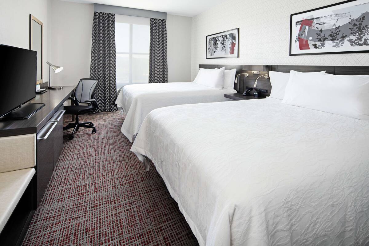 A hotel room with two beds, a desk with a TV, a lamp, and a chair.