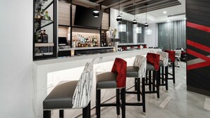 A modern bar area with high stools, a counter with a variety of bottles, and pendant lighting. - Hilton Garden Inn Irvine Spectrum Lake Forest (Lake Forest)