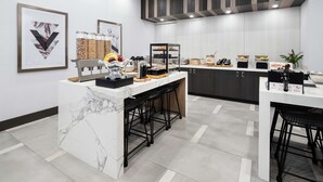 A modern kitchen with marble countertops, black bar stools, and a variety of food items displayed on shelves. - Hilton Garden Inn Irvine Spectrum Lake Forest (Lake Forest)