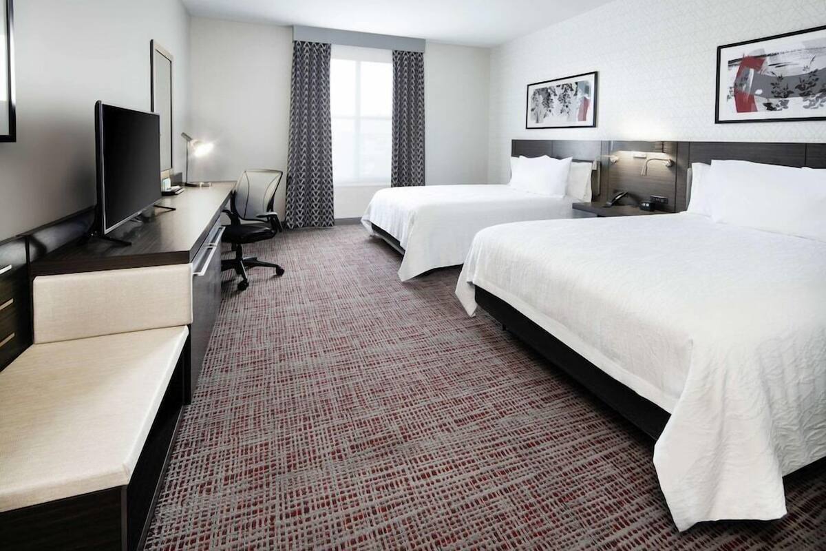 A hotel room with a bed, a desk with a computer, a chair, a TV, and a window with curtains.