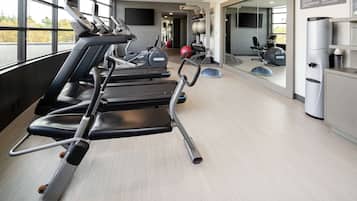 Un gimnasio con cintas de correr, pelotas de ejercicio y un espejo grande.