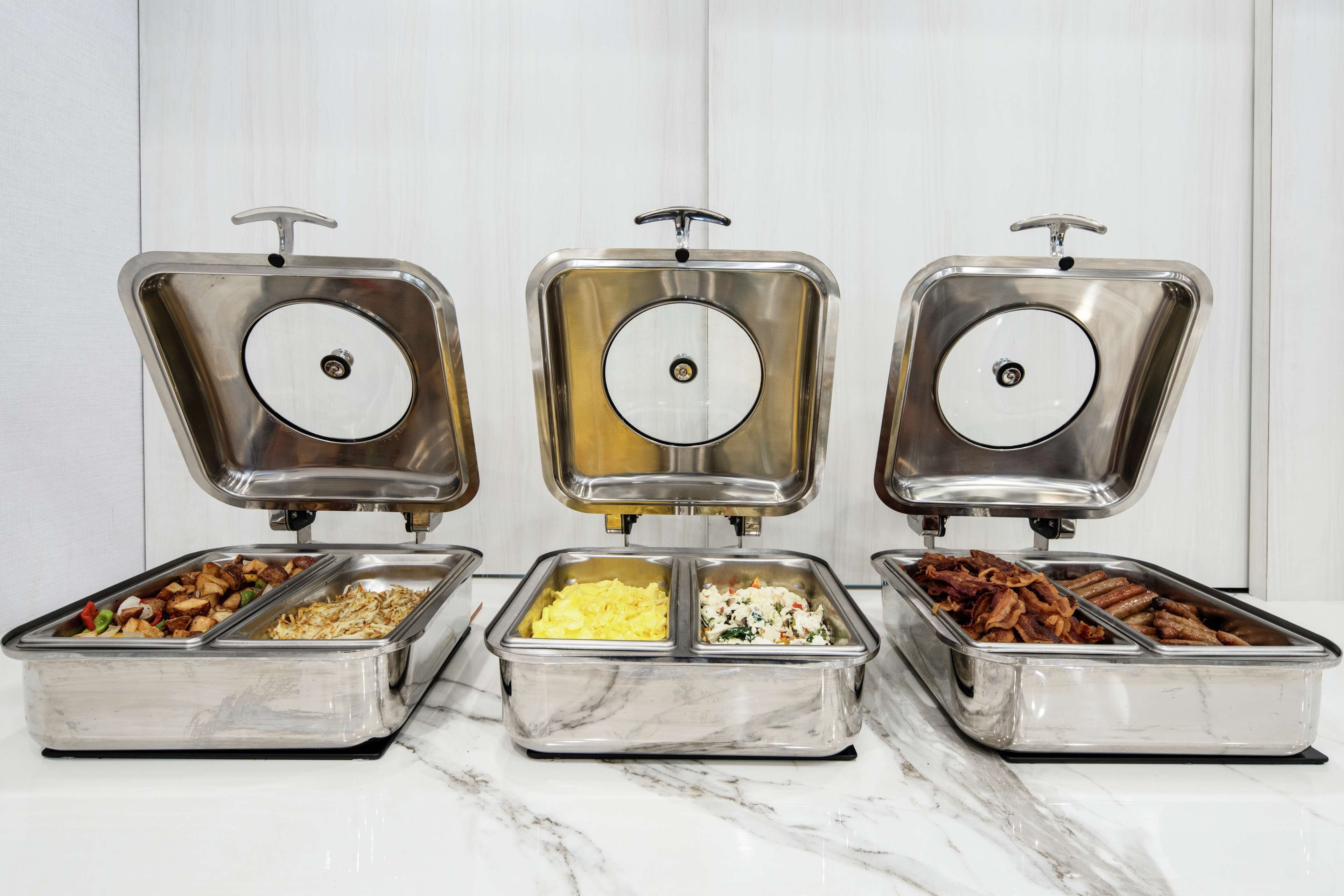Tres contenedores de acero inoxidable para buffet con tapas, cada uno con distintos alimentos.