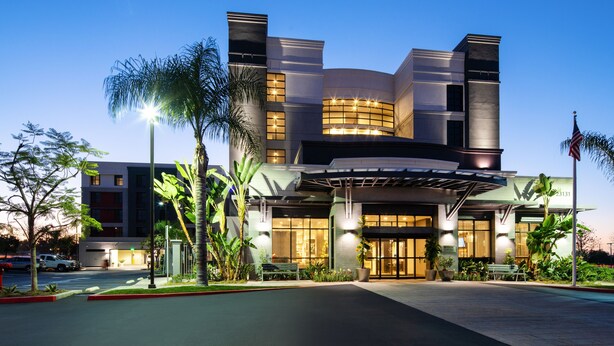 A modern hotel with a curved facade, large windows, and a well-lit entrance. - Hilton Garden Inn Irvine Spectrum Lake Forest (Lake Forest)