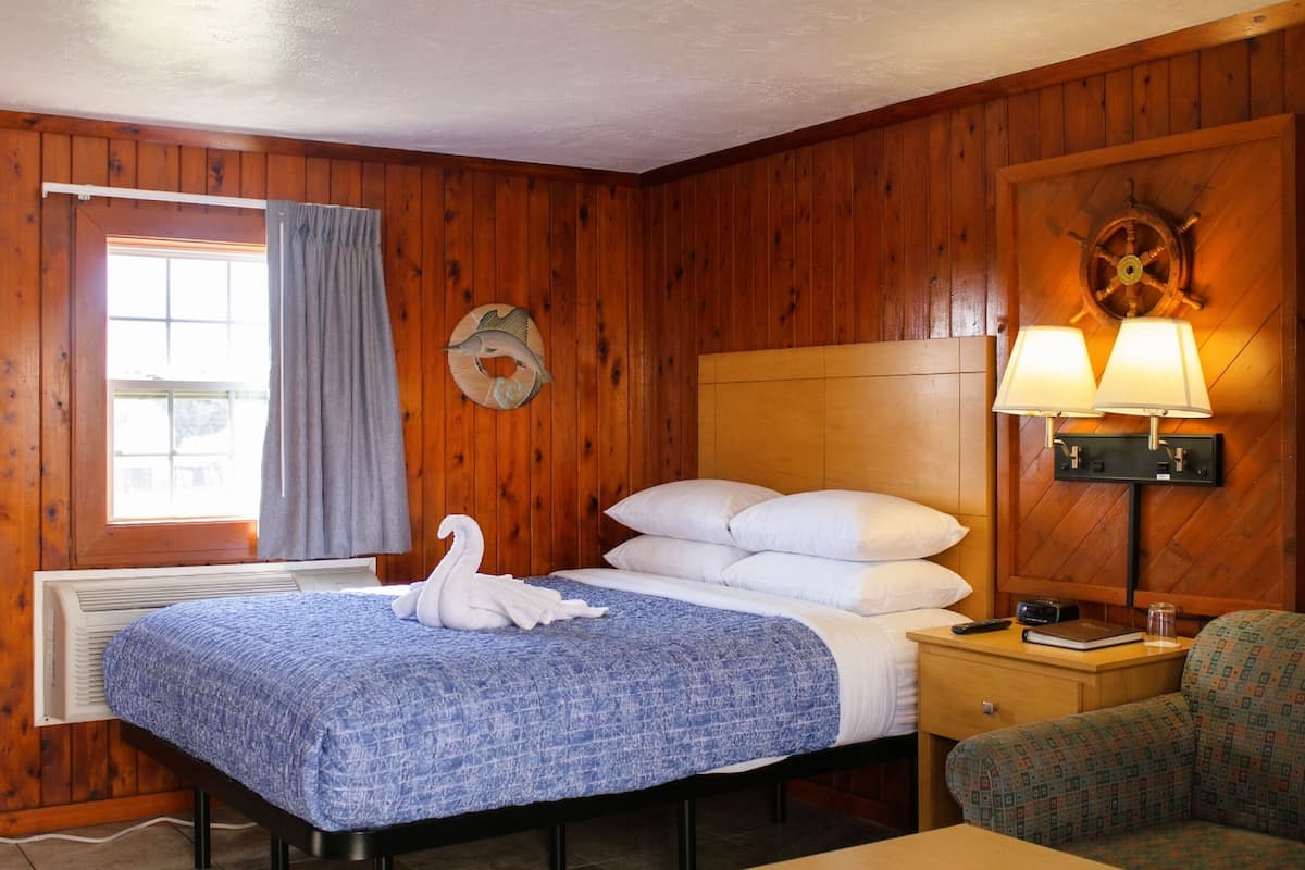 Ein Zimmer mit Holzboden, einem Bett, einem Nachttisch, einer Lampe und einer Wanddekoration.
