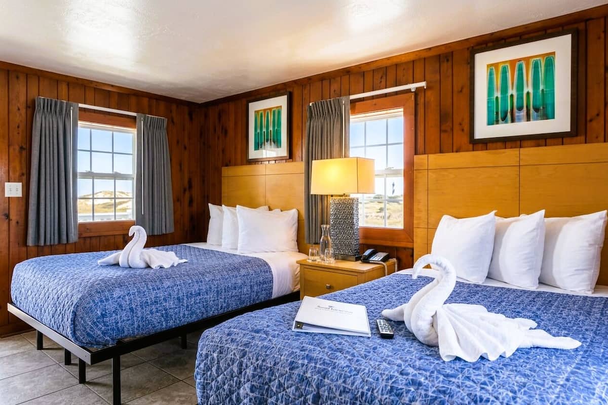 Ein Hotelzimmer mit zwei Betten, Holzvertäfelung, einer Lampe, einem Telefon und einem gerahmten Bild an der Wand.