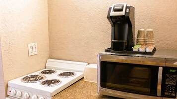 A kitchen with a stove, microwave, coffee maker, and stacked paper cups.