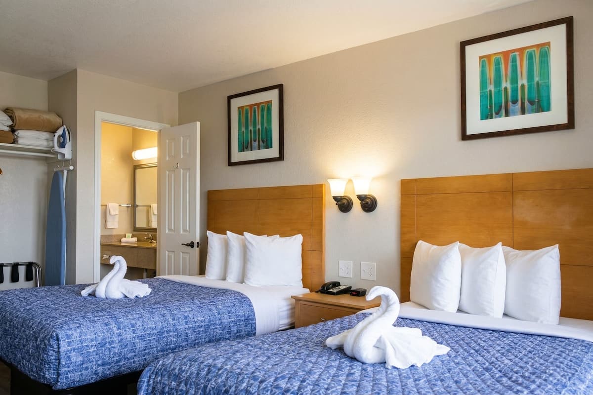 Ein Hotelzimmer mit zwei Betten, einem Holzkopfteil, einem Nachttisch und einem durch eine offene Tür einsehbaren Badezimmer.