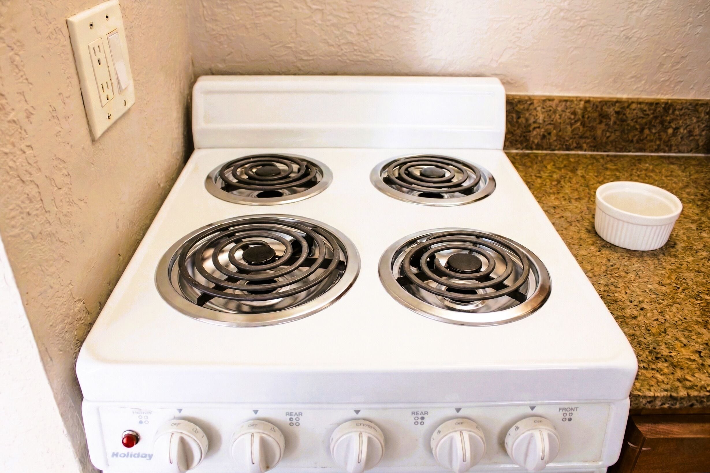 A white stove with four burners and a control panel with knobs and a red button.