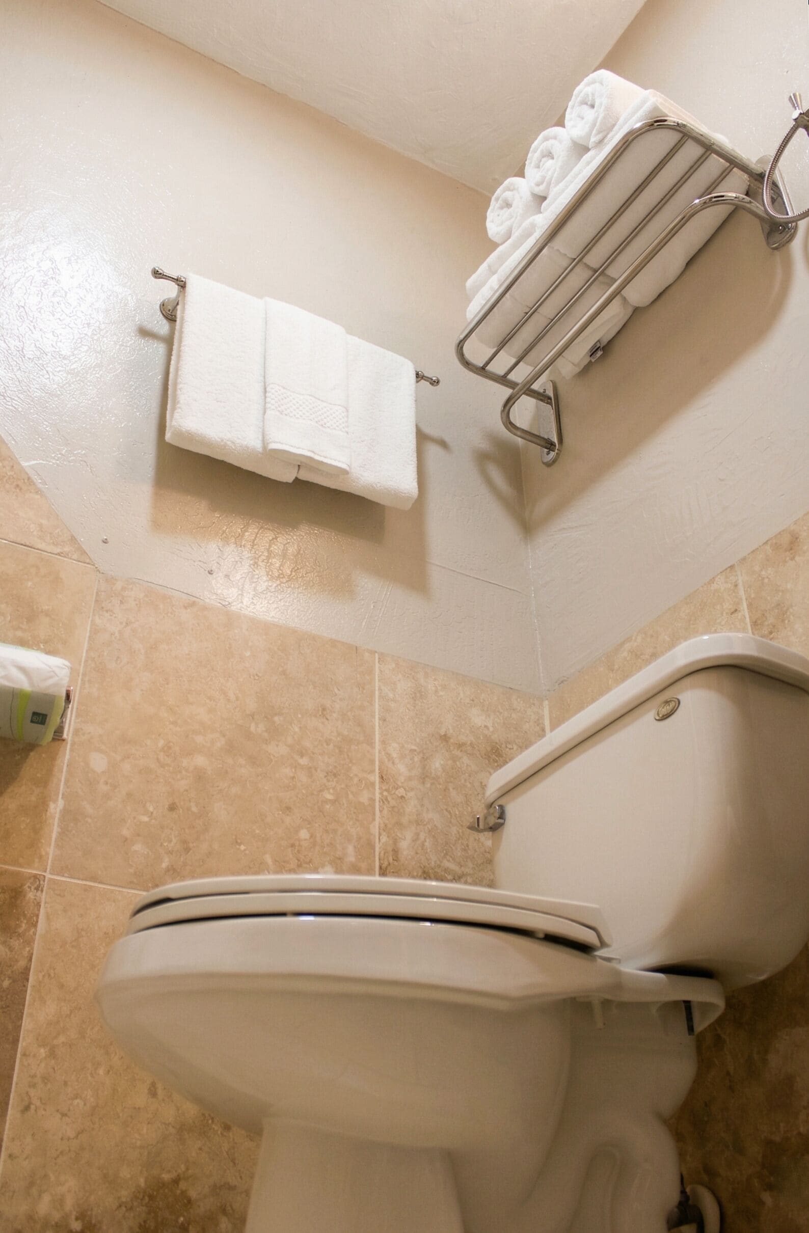 Une salle de bain équipée de toilettes, d’un porte-serviettes avec des serviettes pliées et d’un distributeur de papier toilette.