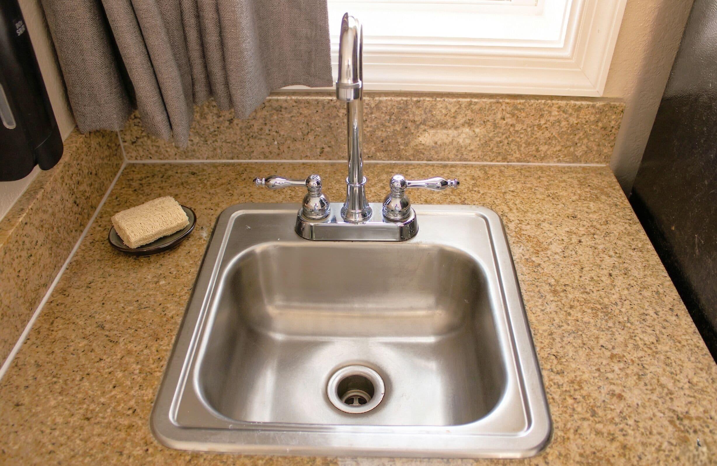 A stainless steel kitchen sink with a single faucet, a soap dish, and a granite countertop.