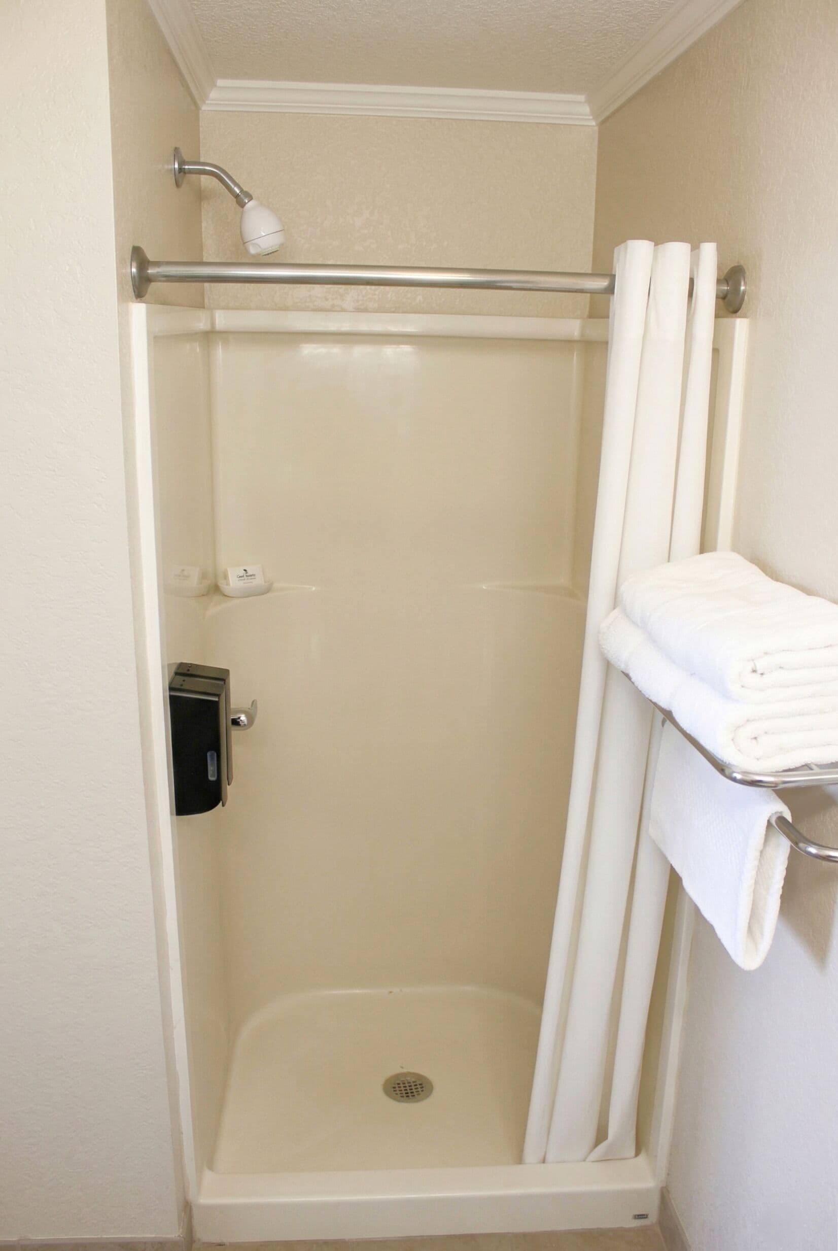 A walk-in shower with a glass door, a hand dryer, and a towel rack with folded towels.