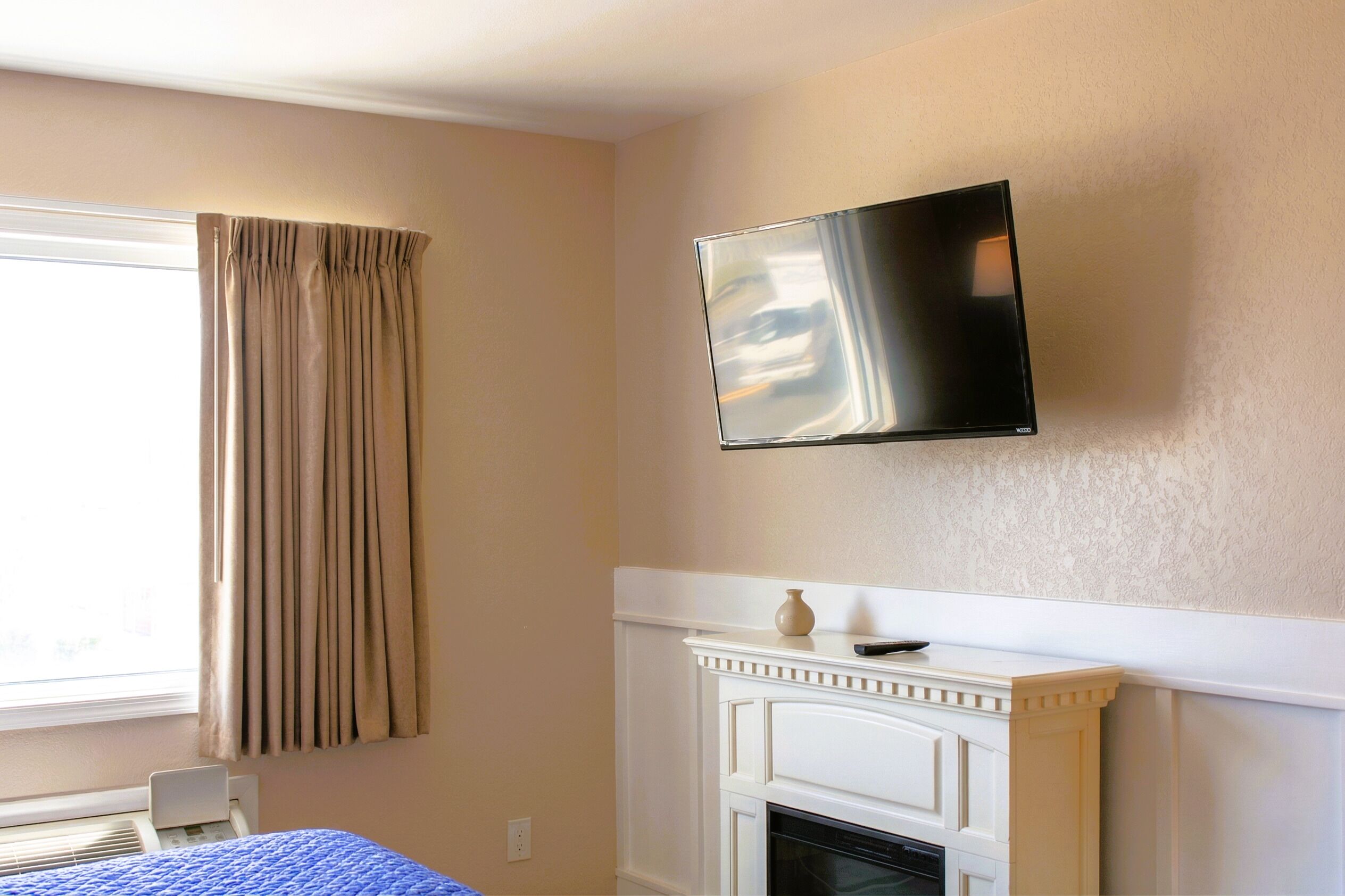 A room with a bed, a television mounted on the wall, a fireplace, and a window with curtains.