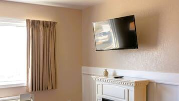 A room with a bed, a television mounted on the wall, a fireplace, and a window with curtains.