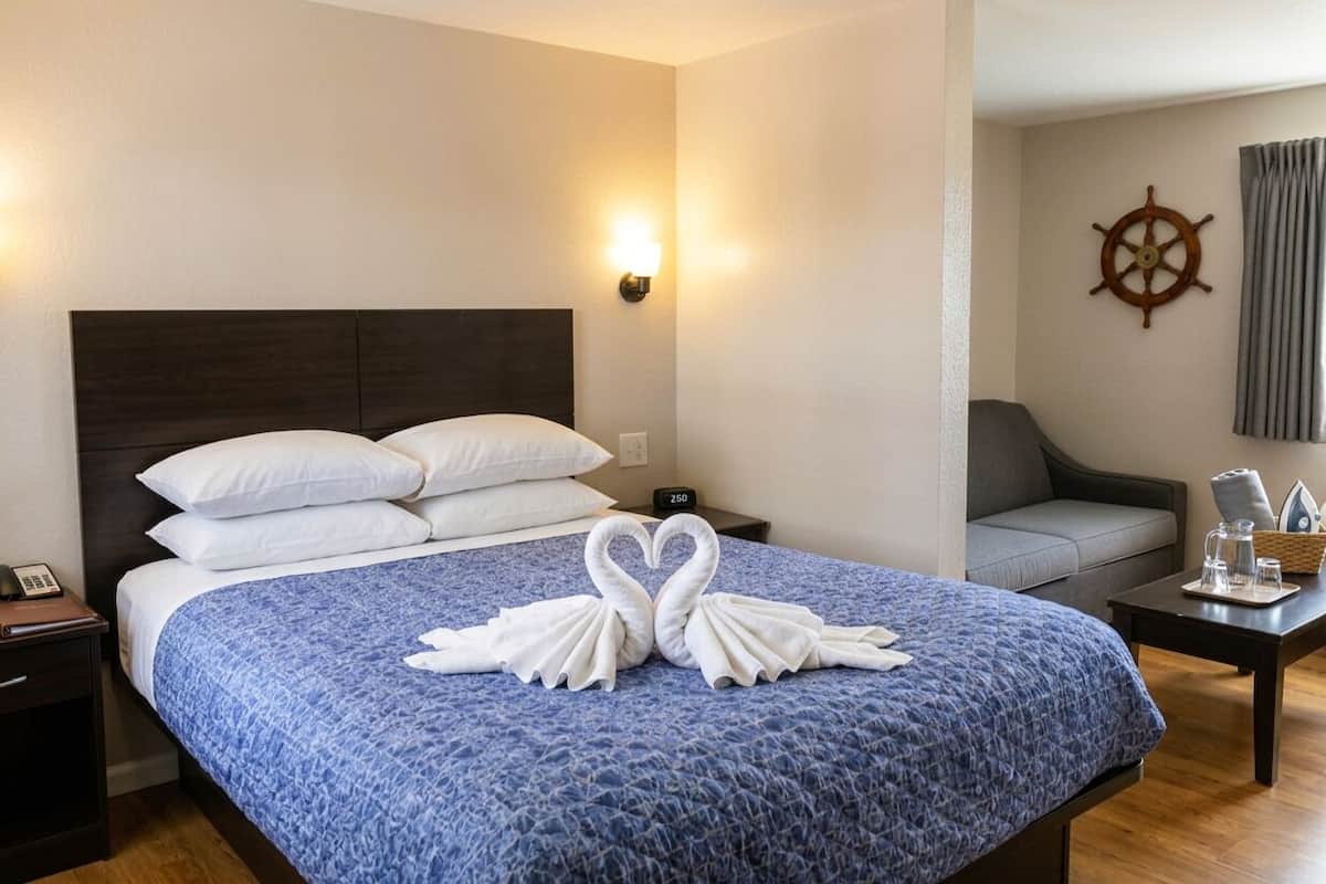 Ein Hotelzimmer mit einem Bett, einem Nachttisch, einem Schreibtisch, einem Stuhl, einer Wanduhr und einer Schiffslenkrad-Dekoration.