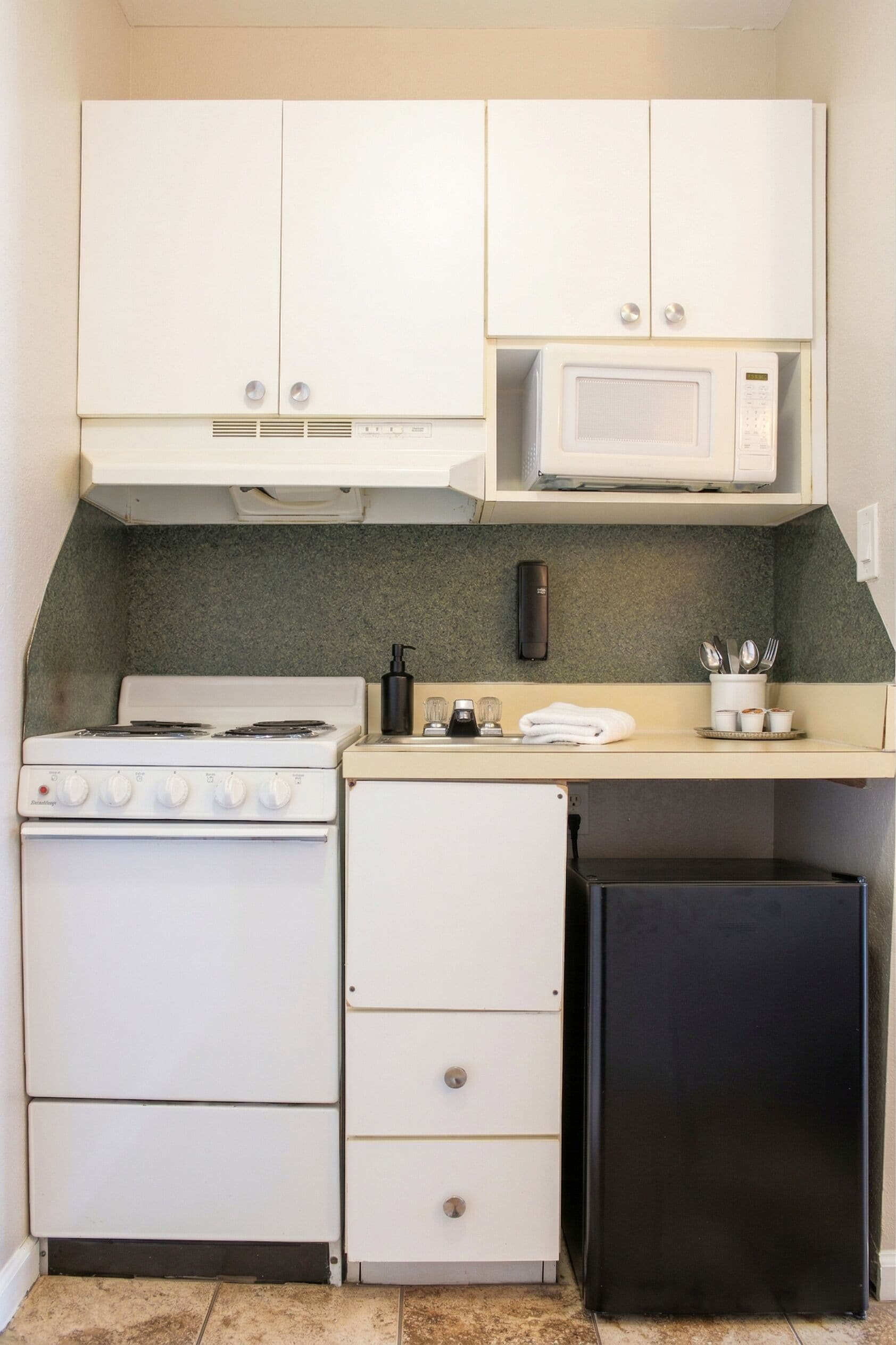 A compact kitchen with a stove, microwave, refrigerator, and a small countertop with a coffee maker and utensils.