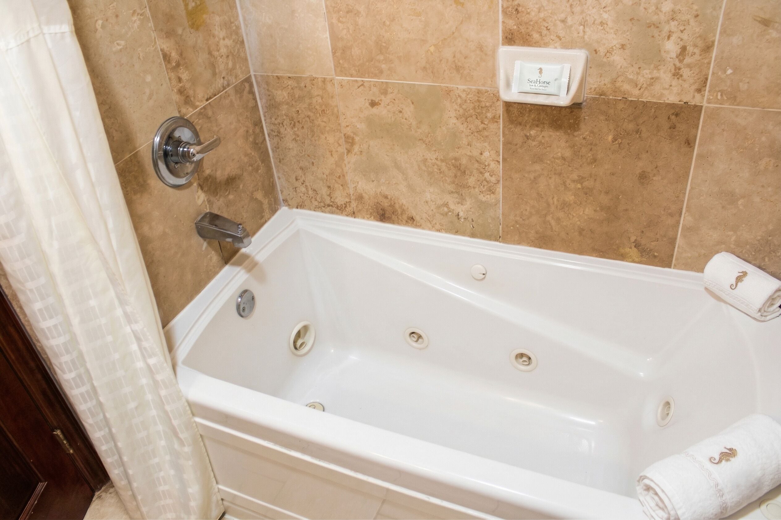 Eine weiße Badewanne mit Duschbrause, Handtuch und Wandseifenspender.