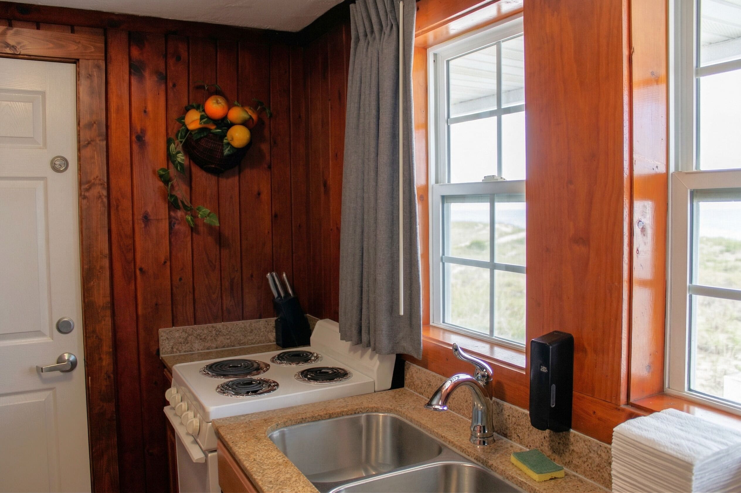 A kitchen with a stove, sink, and window with curtains.