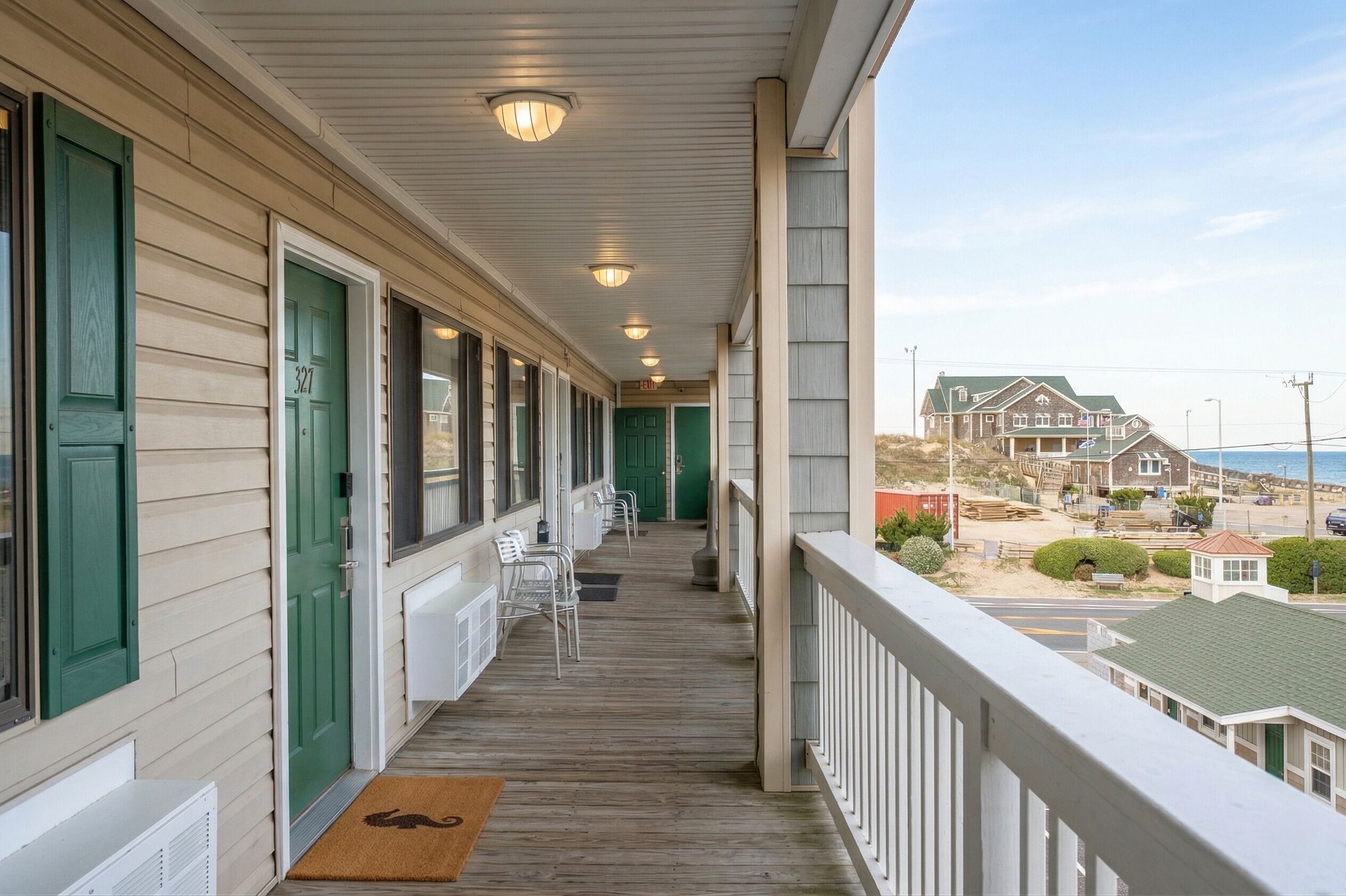 Une véranda couverte avec un plancher en bois, des portes vertes et une vue sur une plage et l’océan.