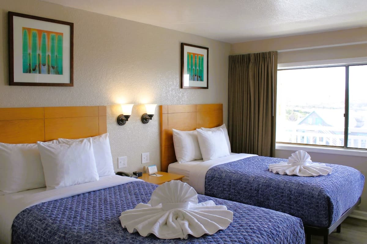 Ein Hotelzimmer mit zwei Betten, einem Kopfteil, Wandleuchten und einem mit Vorhängen versehenen Fenster.