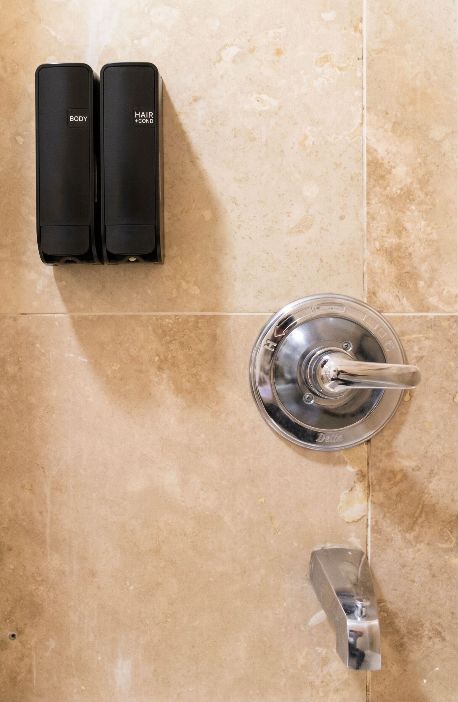 A bathroom with a shower, a sink, and two black hair care products on the wall.