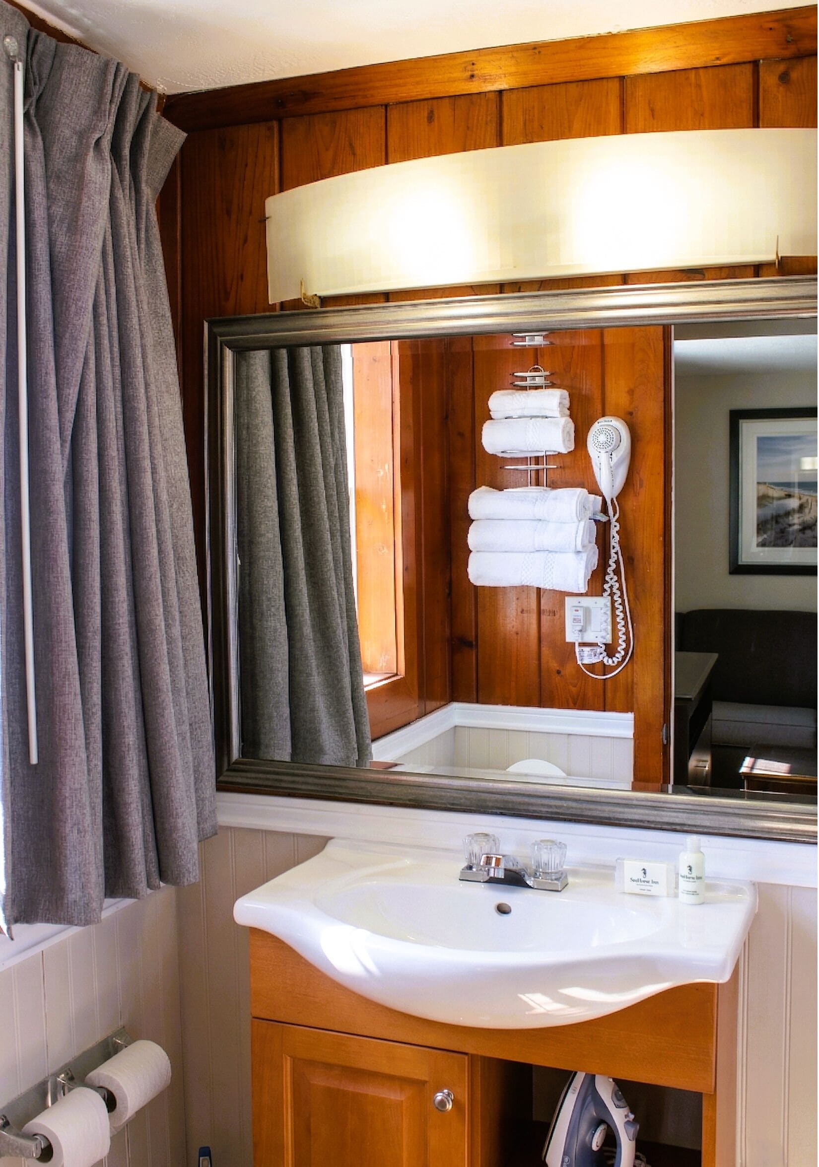 Une salle de bain avec un meuble-lavabo en bois, un évier, un miroir, un porte-serviettes et un sèche-cheveux.