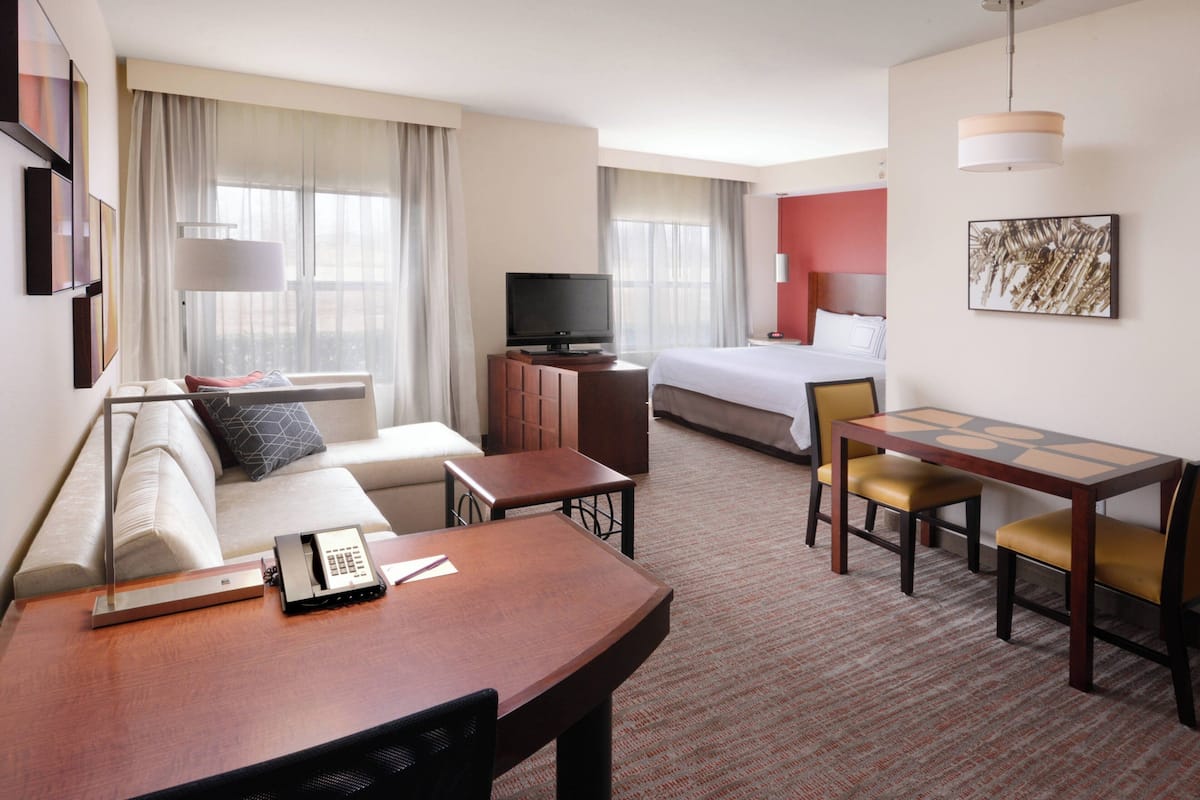 A hotel room with a bed, a sofa, a desk with chairs, a television, and a telephone.