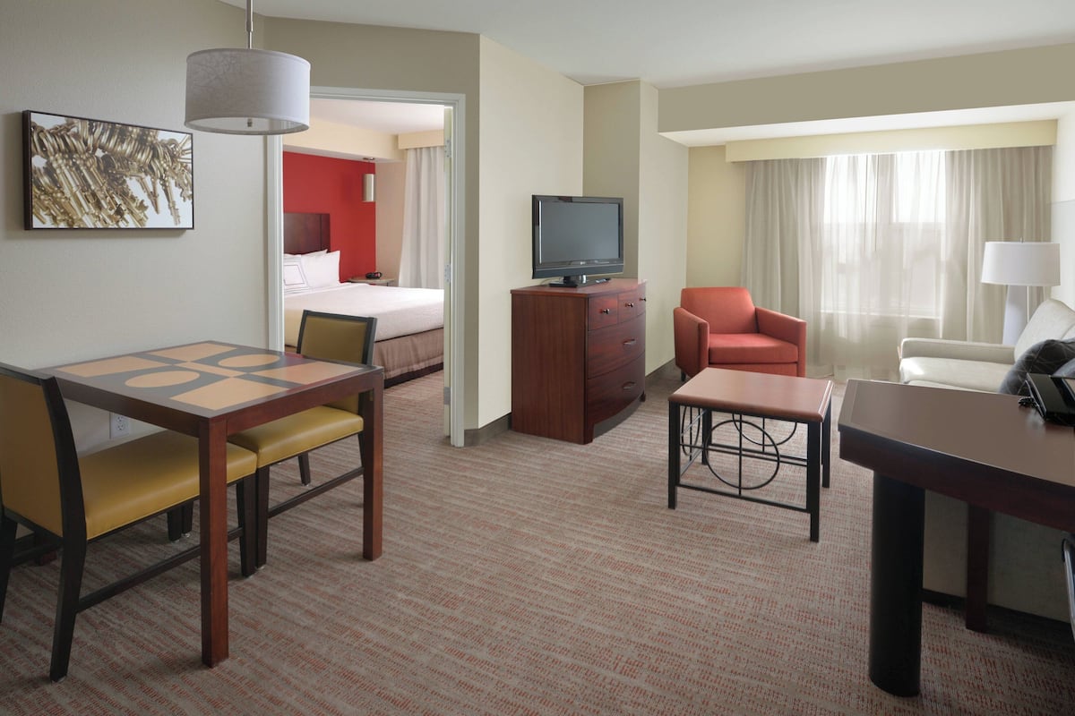 A hotel room with a bed, a TV on a wooden cabinet, a desk with a chair, and a sofa.
