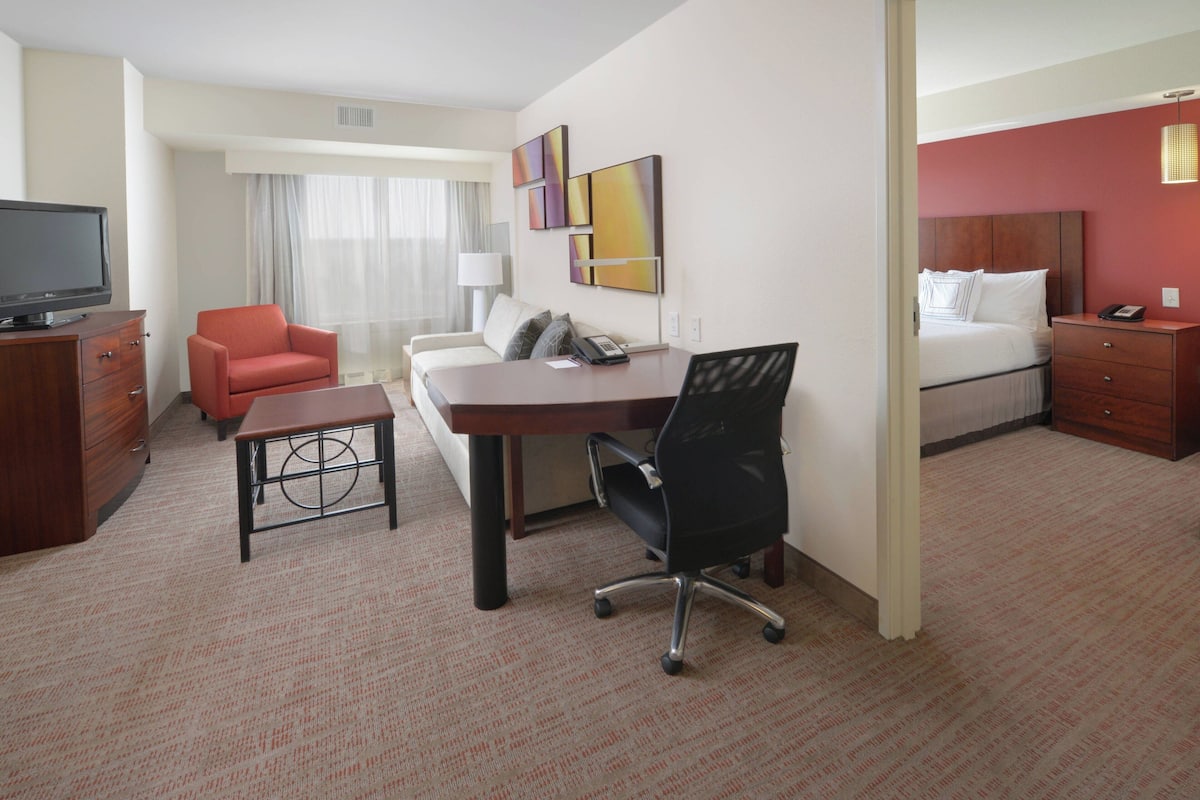 A hotel room with a bed, a desk, a chair, a TV, and a lamp.
