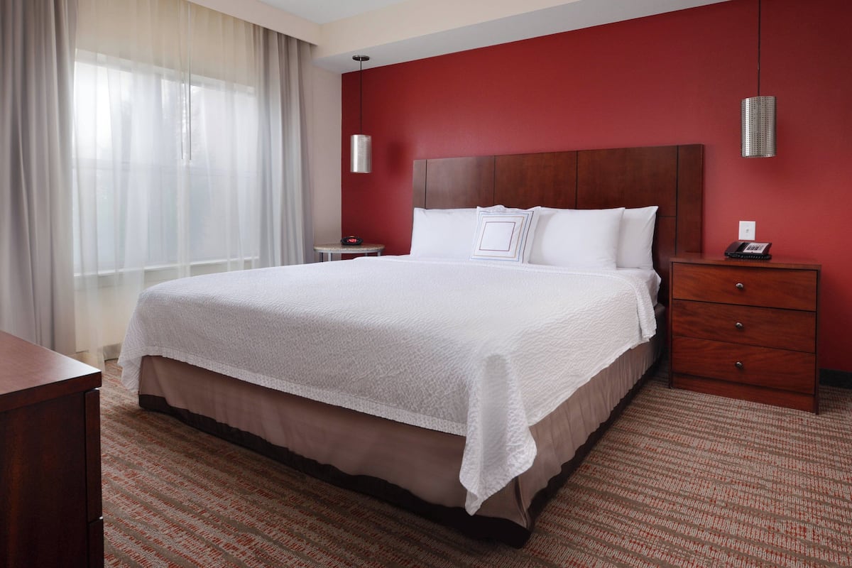 A hotel room with a large bed, a wooden headboard, a bedside table with a lamp, and a nightstand with a phone.