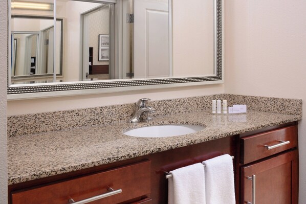 A bathroom with a granite countertop, a sink, a mirror, and wooden cabinets.