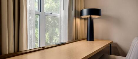 Ein modernes Zimmer mit einem Holztisch, einer schwarzen Lampe und Blick ins Grüne durch ein Fenster.