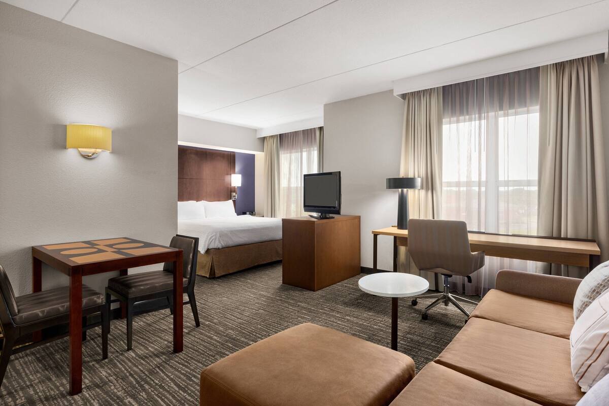 A hotel room with a bed, a desk, a TV, a sofa, and a small table with chairs.
