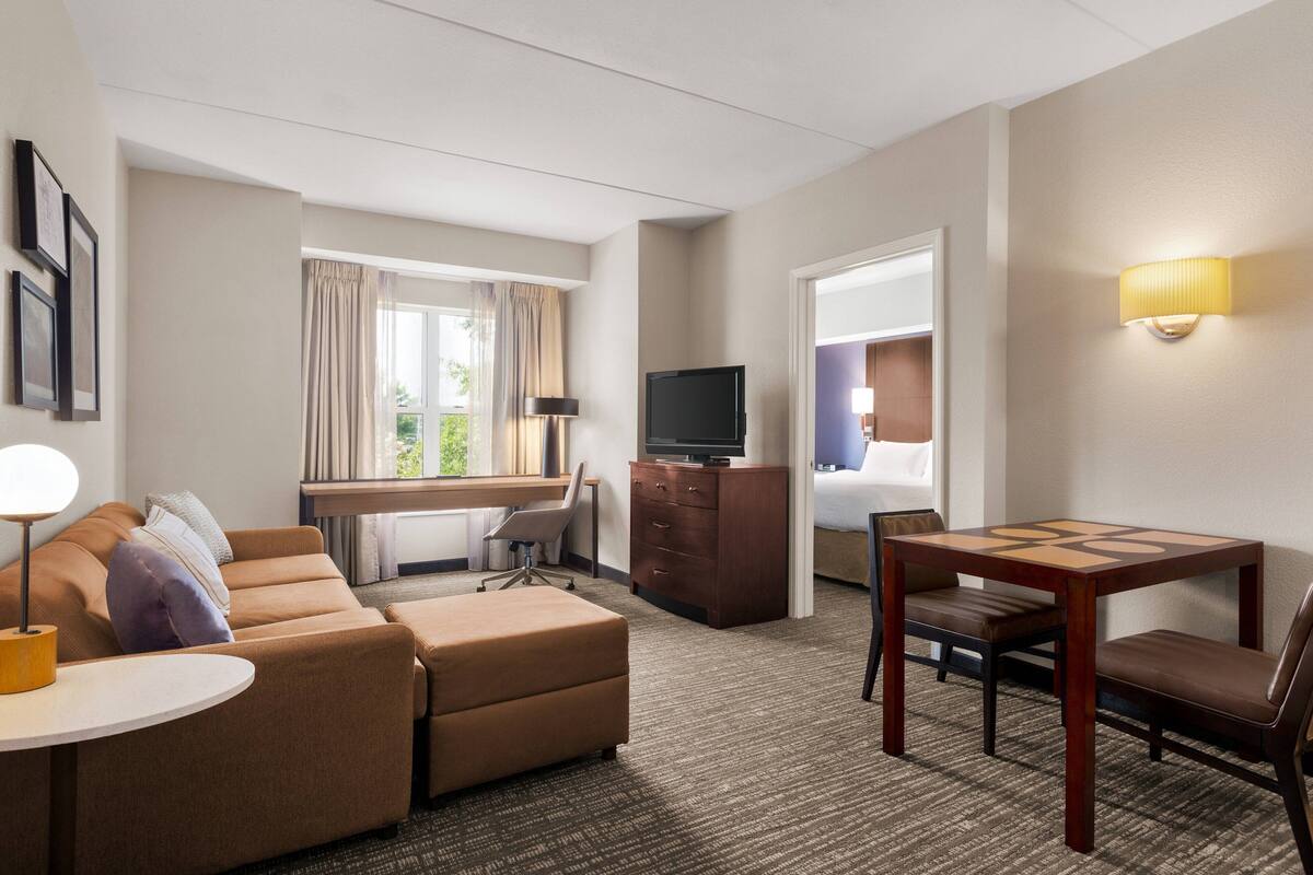 A hotel room with a sofa, a desk, a television, a bed, and a small table.