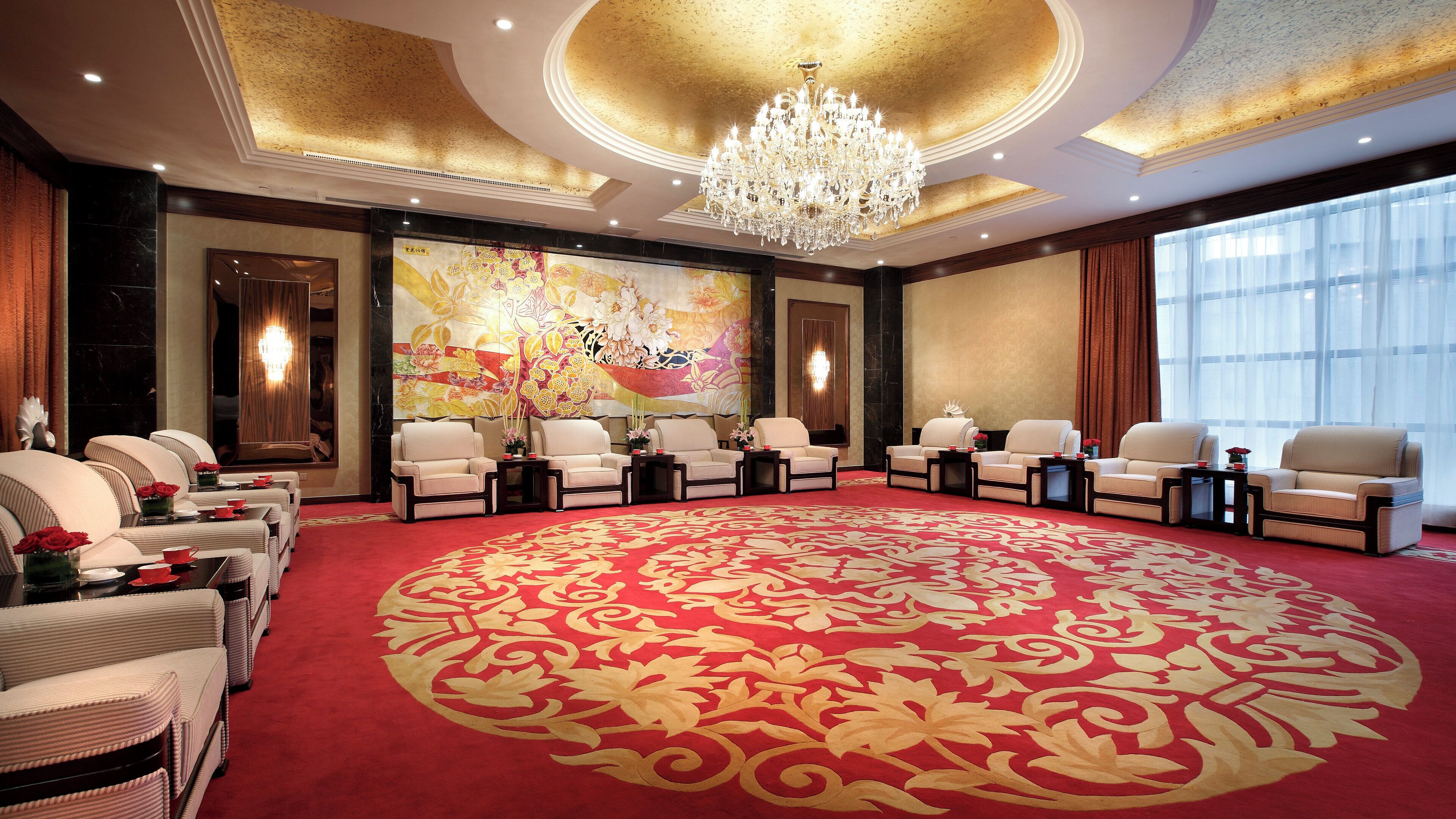 Habitación de hotel con una alfombra redonda grande, un candelabro y un cuadro floral de gran tamaño en la pared.