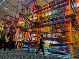 An indoor play area with colorful climbing structures and netted obstacles.