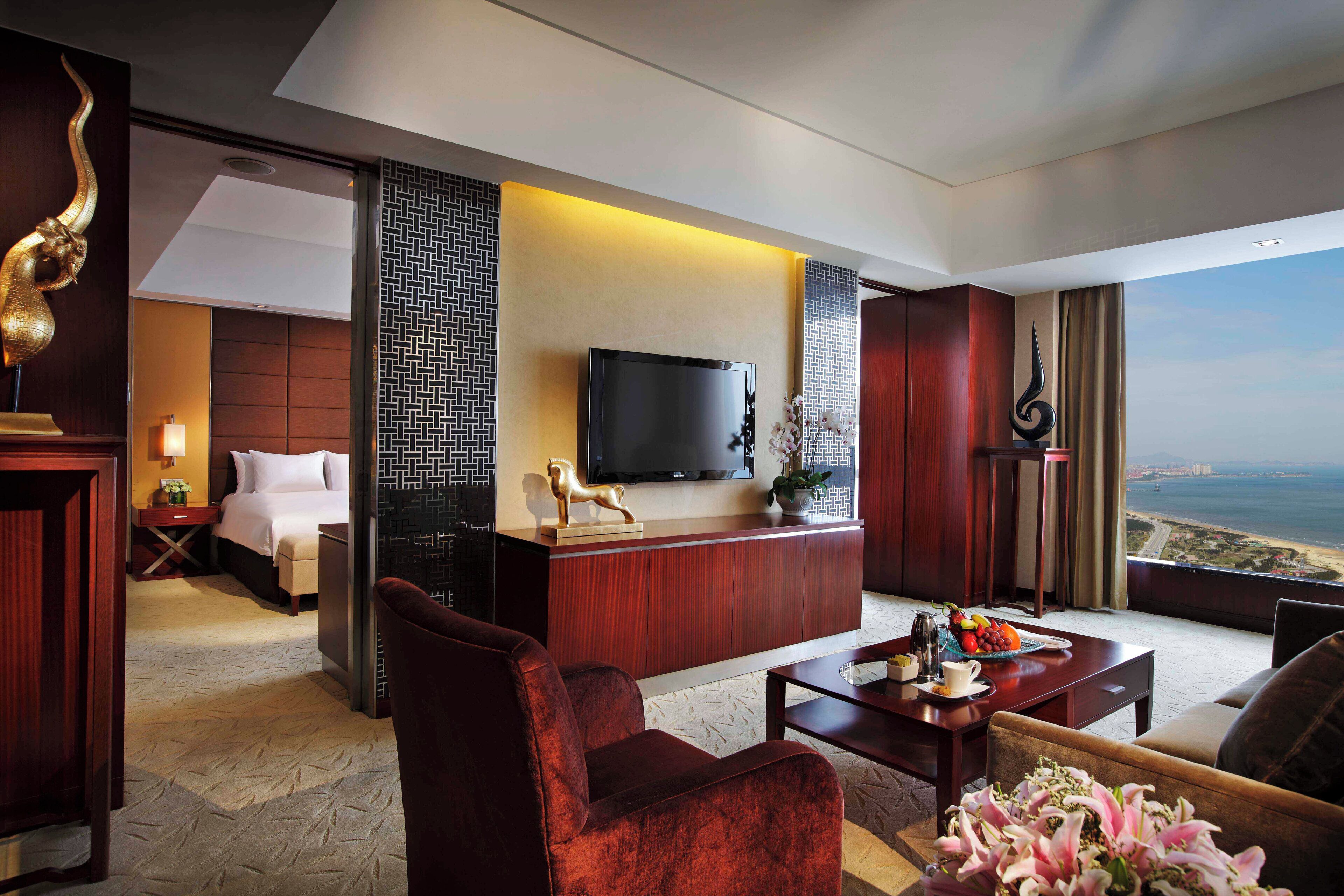 A hotel room with a bed, a desk, a TV, a view of the sea, and a large window.
