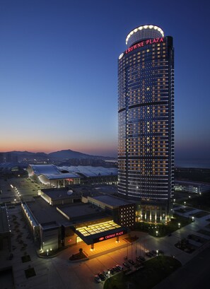 Un hôtel de grande hauteur, reconnaissable à son grand panneau « CROWNE PLAZA », doté d’une façade moderne en verre et d’un vaste parking.