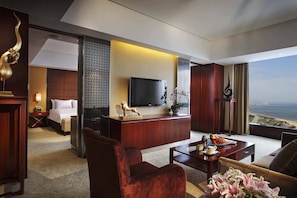 A hotel room with a bed, a desk with a flat-screen TV, a seating area with a coffee table, and a view of the ocean. - Crowne Plaza Yantai Seaview by IHG (Yantai)