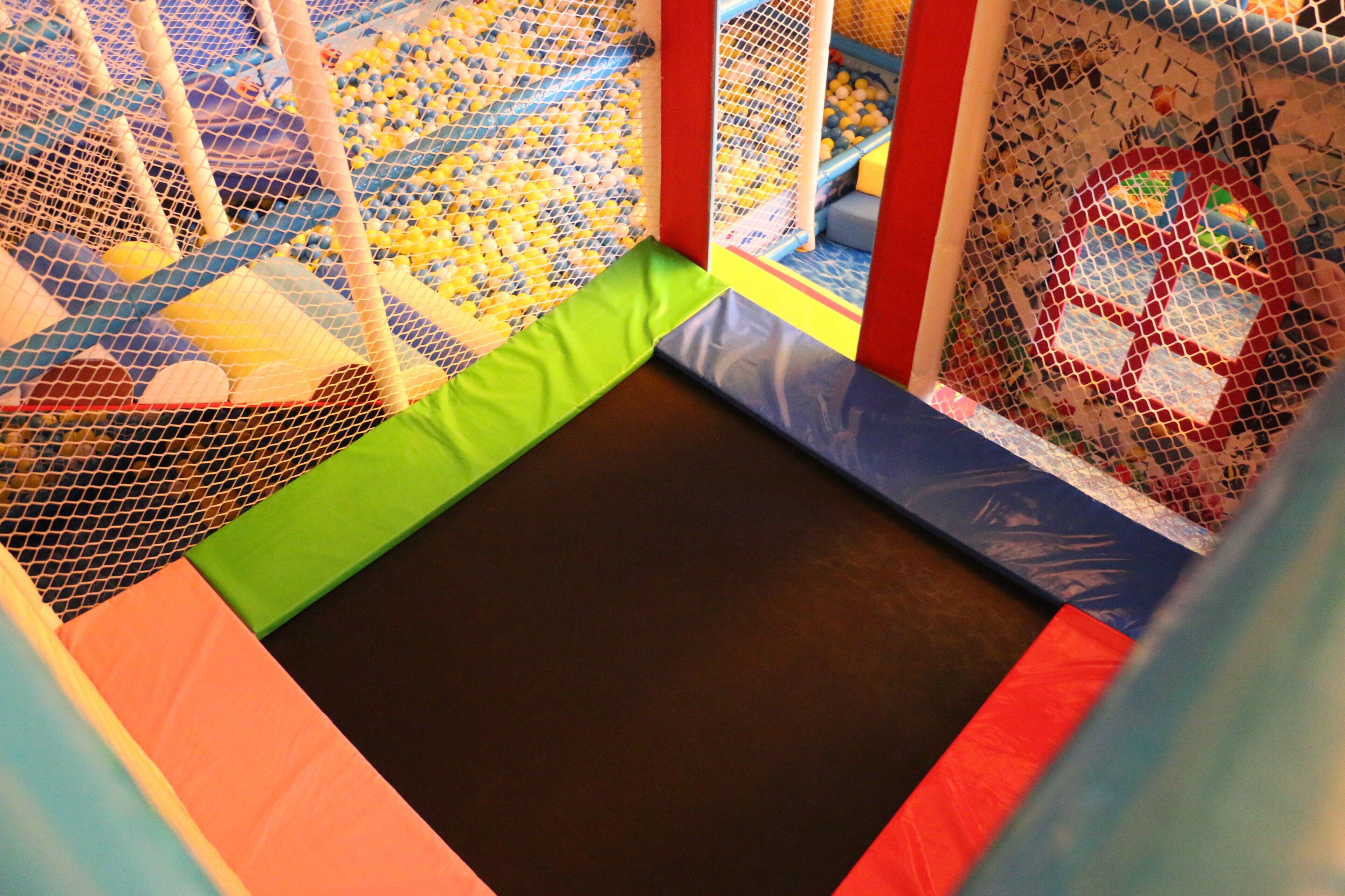 A multi-level indoor play area with netted climbing walls and padded surfaces.