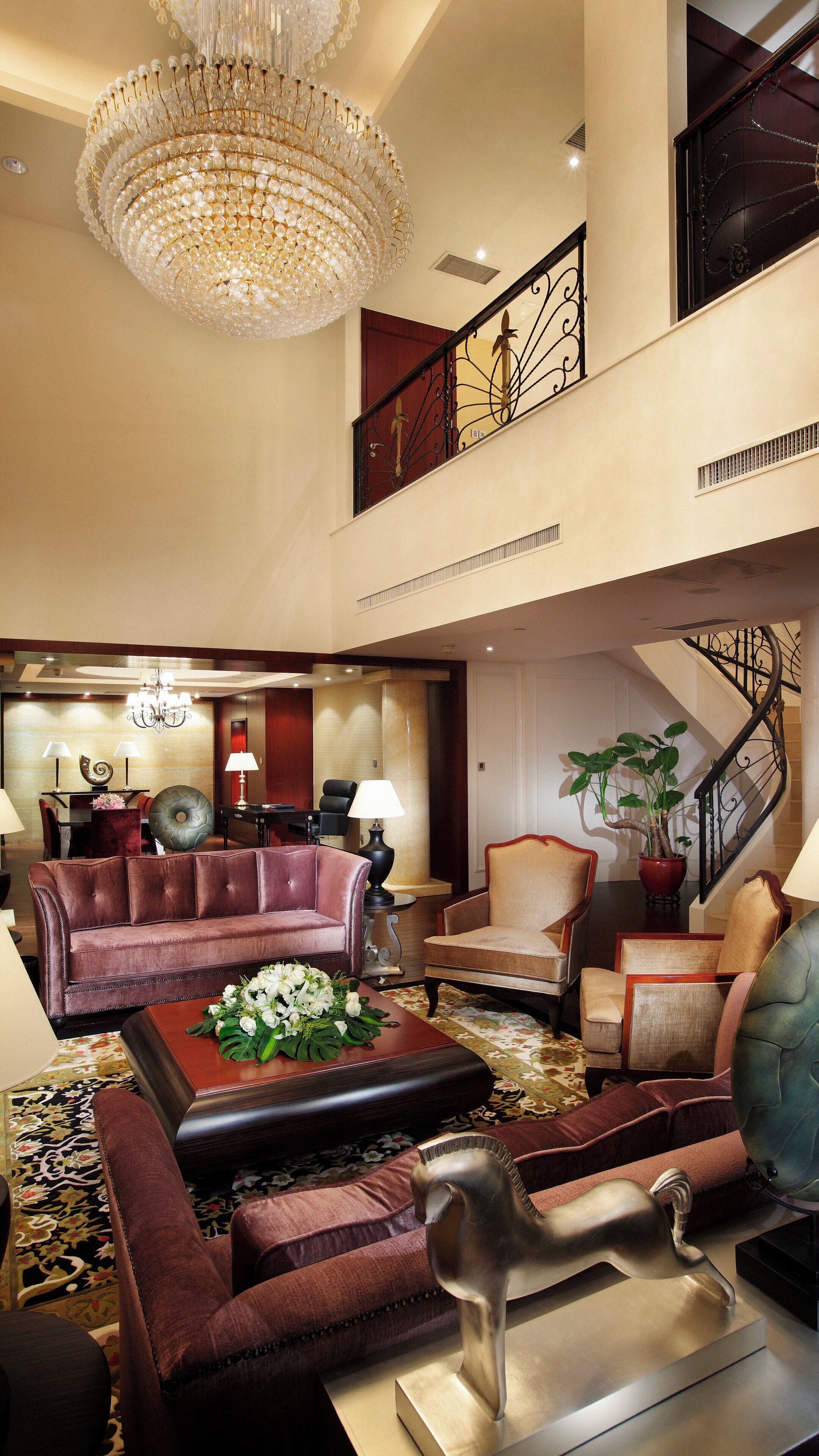 A spacious lobby with a grand chandelier, a staircase, and a seating area with a coffee table and chairs.