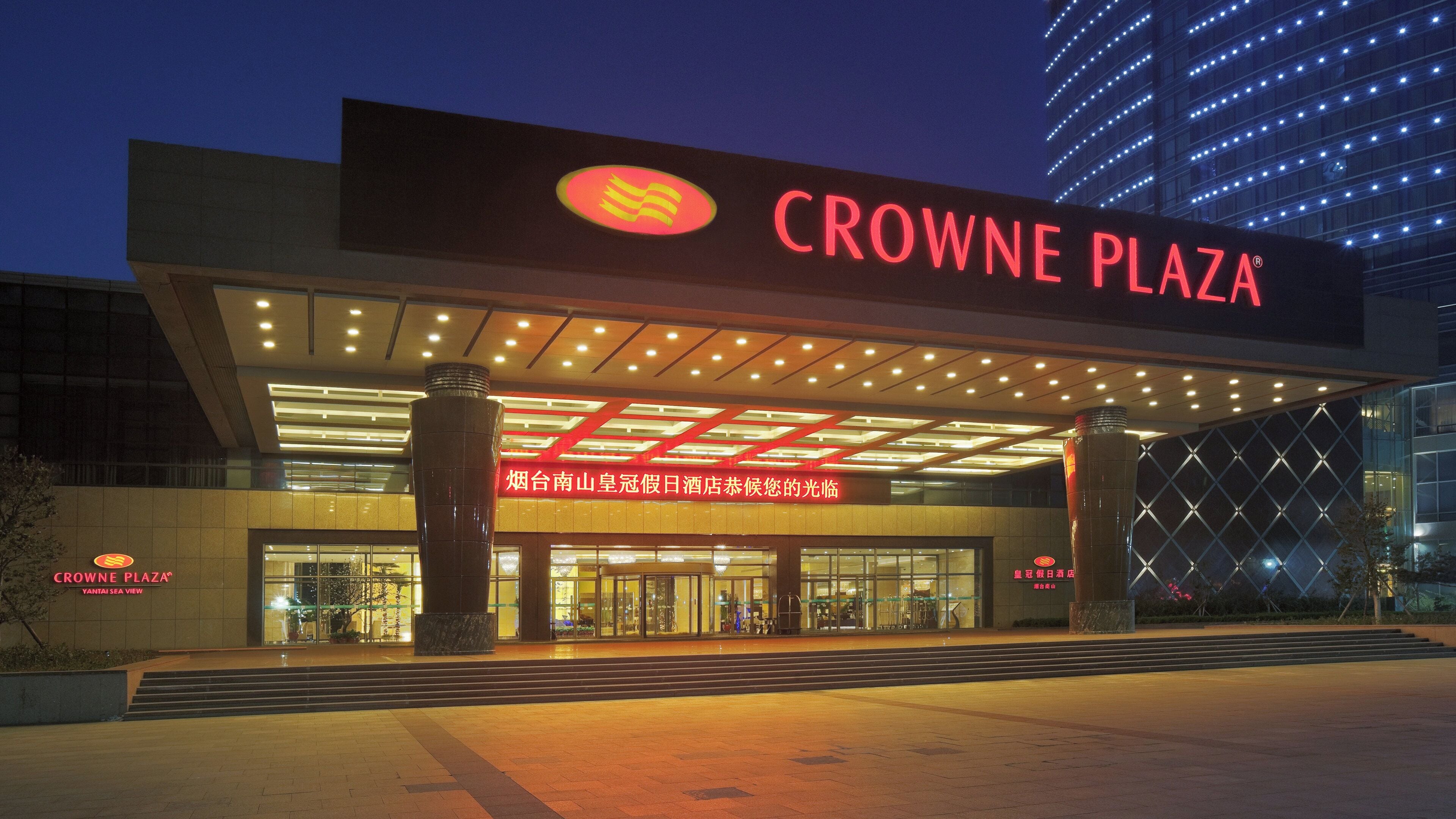 Exterior del hotel Crowne Plaza, con una entrada destacada y señalización iluminada.