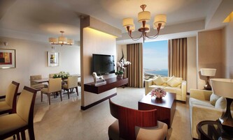 Habitación de hotel con televisión, zona de estar, mesa de comedor y vista al mar.
