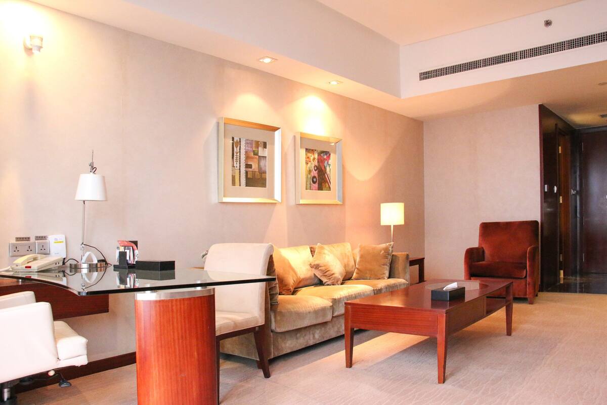 A modern hotel lobby with a reception desk, a sofa, a coffee table, and a red armchair.