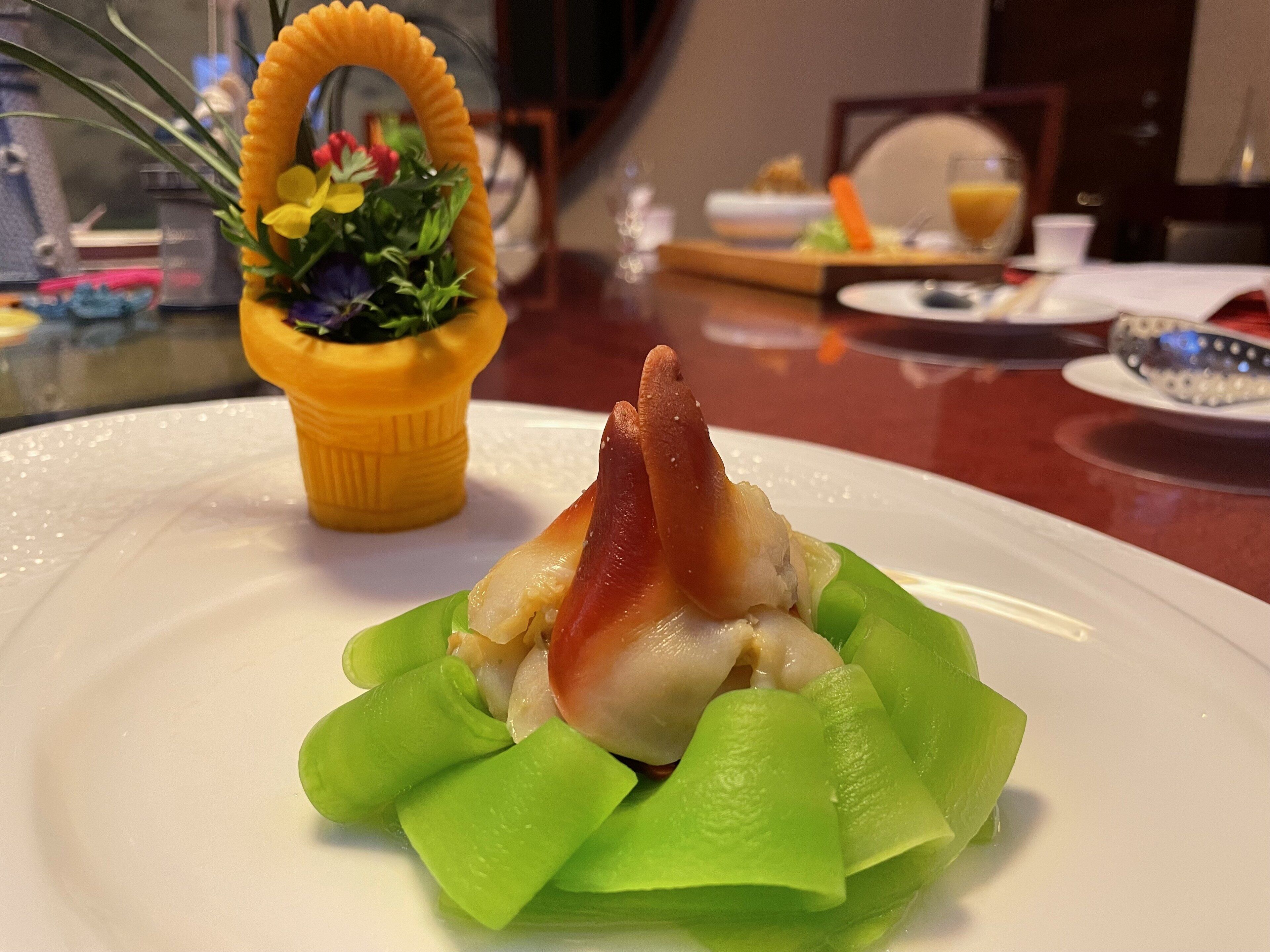 A plate with a green vegetable base, a piece of meat, and a yellow container with flowers.