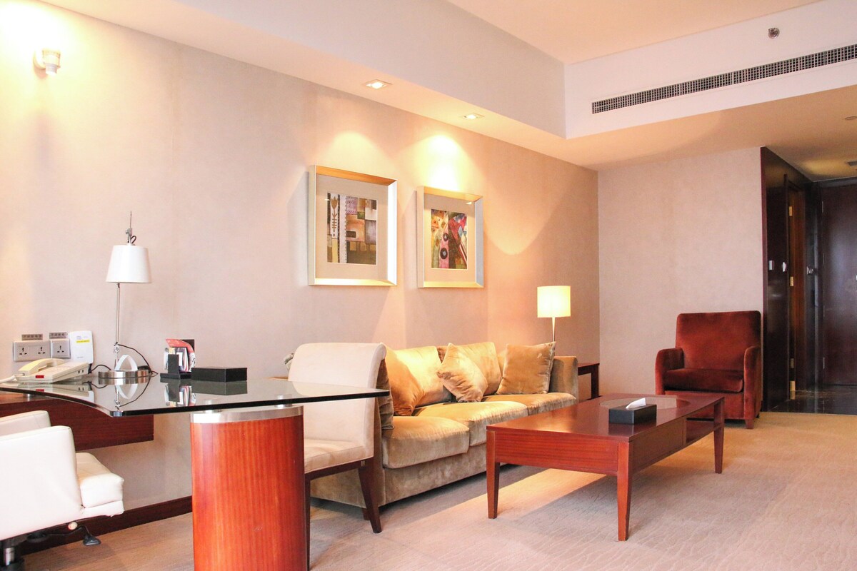 A modern hotel lobby with a reception desk, a sofa, a coffee table, and a red armchair.