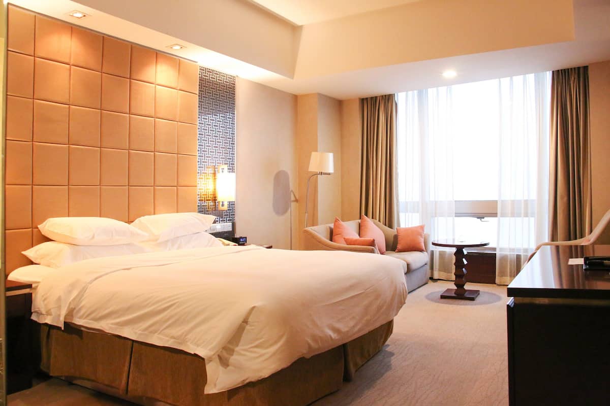 A hotel room with a large bed, a desk, a chair, a lamp, and a window with curtains.
