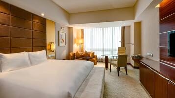 A hotel room with a large bed, a desk, a chair, and a TV.