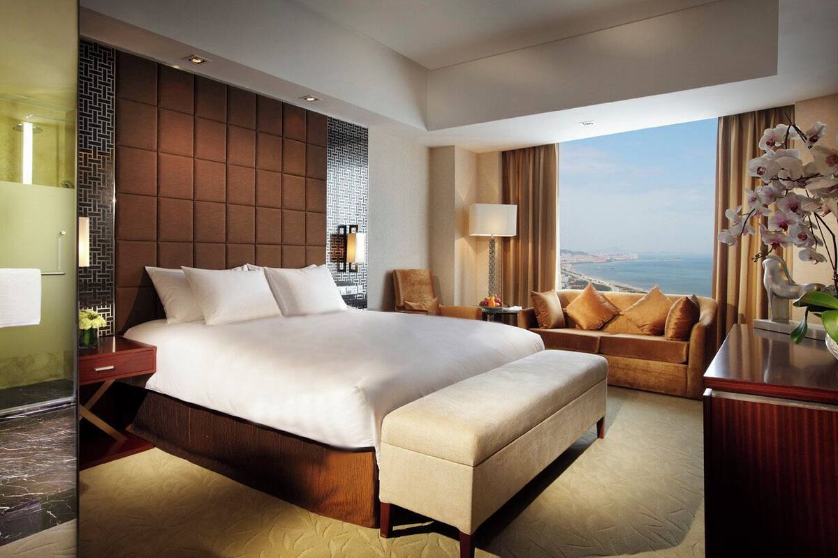 A hotel room with a large bed, a sofa, a desk, and a view of the sea.